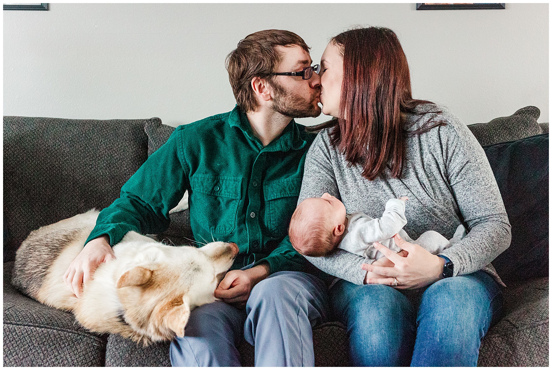 Parents kissing on couch with dog and newborn baby